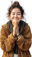 Smiling young woman expressing gratitude with hands together, wearing a cozy brown sweater in a bright outdoor setting during daytime photo