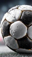 Detailed close-up view of a wet soccer ball with droplets and shiny surface on a field during a rainy day photo