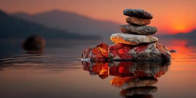 Stacked stones reflect vibrant sunset colors on tranquil water surface in peaceful landscape photo