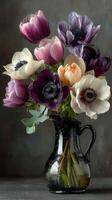Colorful anemones arranged in a vintage black pitcher on a solid background in a softly lit setting photo