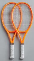 Two vibrant orange tennis rackets positioned on a neutral background ideal for sports apparel and equipment promotions photo