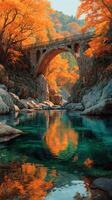 Colorful autumn foliage surrounds a stone bridge over a tranquil stream in a scenic landscape during early morning light photo