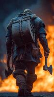 Warrior walking away from the flames, carrying axes and a heavy backpack in a rugged landscape at dusk photo