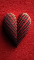 Heart-shaped decorative object with red and black stripes placed on textured red background photo