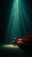 Lonely figure seated in an empty theater under a bright spotlight with red chairs in the background photo