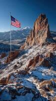 Majestic American flag waves atop snowy rocks with mountains in the background during a clear day photo