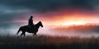 Cowboy riding horse against sunset in misty landscape with tall grass photo