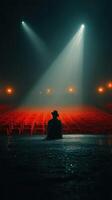 Seated figure observing empty theater under soft stage lights during a hazy evening photo