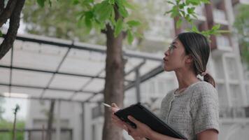 hembra científico examina un árbol en un urbano configuración, su mirada fijo atentamente en sus hojas, destacando el crucial papel de ambiental observación en moderno paisajes urbanos. video