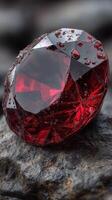 Sparkling red gemstone resting on textured dark stone surface with water droplets in natural lighting photo