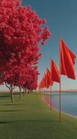Bright red flags line a tranquil lakeside path adorned with vibrant blooming trees under a clear blue sky photo