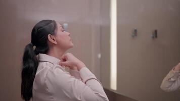 Reflection in the mirror A woman is adjusting the collar of her shirt while looking in the mirror. It is a quiet moment of self-assessment, preparing for the day ahead. It is a portrait video