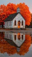 Old church surrounded by vibrant autumn trees reflecting in calm water during sunset photo