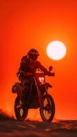 Motorcycle rider navigating sandy terrain during sunset with a vibrant orange sky photo