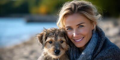 Woman enjoys a sunny day by the water with her playful dog on the shore during autumn afternoon photo