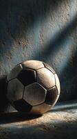 Vintage soccer ball resting against a textured wall in soft light highlights its worn features and history photo