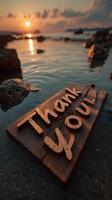 Sunset over the ocean with a wooden sign expressing gratitude placed on the shoreline photo