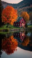 Autumn colors reflect in calm waters near a cozy red house surrounded by vibrant foliage in a serene landscape photo