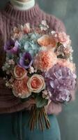 Colorful floral bouquet held by person in cozy sweater against a textured backdrop photo