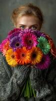 Woman holding a vibrant bouquet of colorful gerbera daisies with a cozy sweater in an artistic indoor setting photo