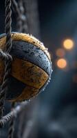 Weathered volleyball hanging from a rope with a blurred background of soft glowing lights in a dramatic setting photo