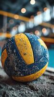 Old volleyball resting on sandy surface in a gym setting with blurred background lights captured at an indoor sports facility photo