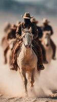 Horse riders lead a herd through dusty terrain at sunset while dressed in cowboy attire photo