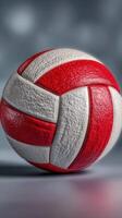 Red and white volleyball sits on a smooth surface in a studio setting with blurred background focus and soft lighting photo