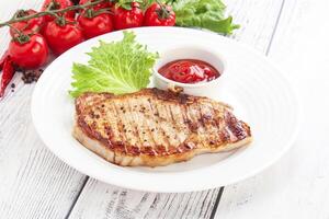 Grilled pork steak with tomato sauce on white plate photo