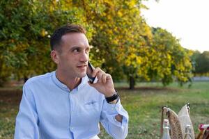 Young smiling man in his thirties while picnicking in the park makes a phone call photo
