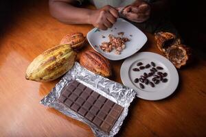 Portrait of a table with the hands of a woman who opens cocoa beans during processing to obtain cocoa for making chocolate. Focus on the chocolate bar. photo
