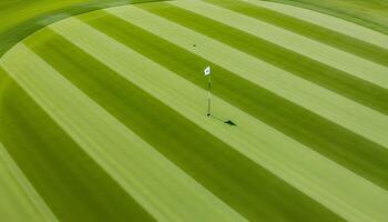 Aerial view of a pristine golf course with striped grass patterns and a small flag marking the hole photo
