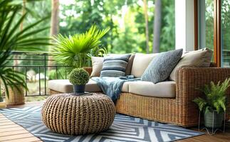 Cozy outdoor terrace with woven rattan sofa adorned with neutral-toned pillows and soft throw blanket, surrounded by lush greenery. Serene setting invites relaxation and leisure in photo