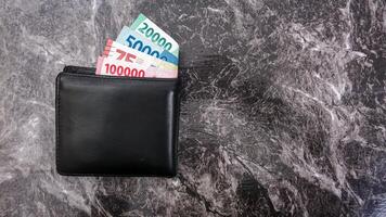 Yogyakarta, Indonesia, 2025 - Black wallet with several Indonesian Rupiah banknotes with different values in it isolated on pattern background photo