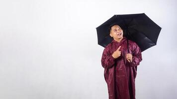 Smiling Asian man in red raincoat holds umbrella and looking up to the sky isolated on white background photo