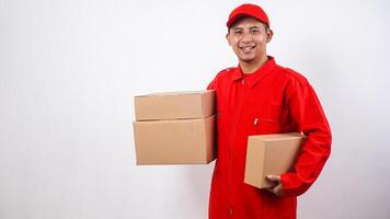 Smiling Asian Delivery man in red uniform carrying package boxes parcel isolated on white background photo