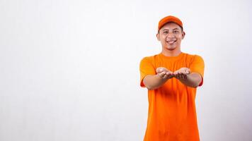 Asian deliveryman in orange t-shirt uniform poses as if he is giving package box to customer isolated on white background photo