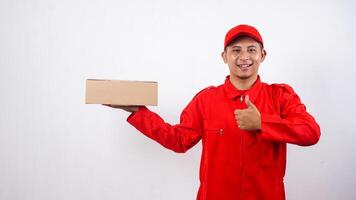 Asian Delivery man in red uniform with package box parcel and showing thumb up isolated on white background photo