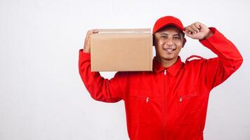 Delivery man in red uniform carrying stack of package box parcel on his shoulder while touching his cap visor isolated on white background photo