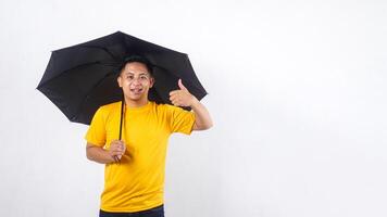 Asian man holding an umbrella and raising his thumb up isolated on white background photo