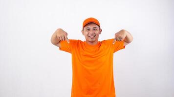 Asian deliveryman in orange t-shirt uniform poses as if he is pointing something bellow isolated on white background for advertisement concept photo
