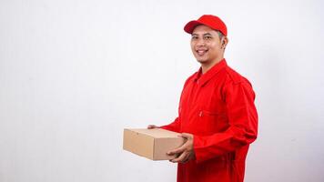 Smiling Asian Delivery man in red uniform holding package box parcel isolated on white background photo