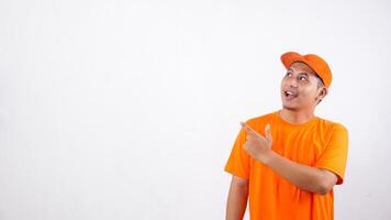 Portrait of Asian deliveryman in orange t-shirt uniform poses as if he is pointing something in empty space area isolated on white background photo