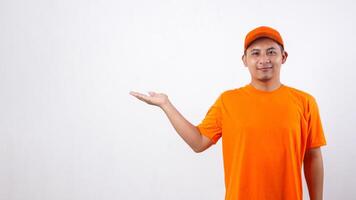 Asian deliveryman in orange t-shirt uniform poses as if he is presenting something in copy space area isolated on white background photo