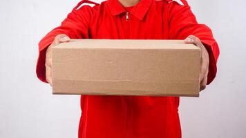 Close up of delivery man in red uniform holding a package box parcel to give to customer isolated on white background photo