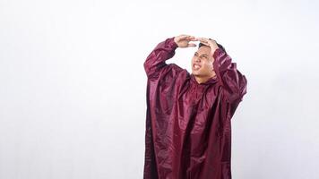 Asian man in red raincoat covering his head with hands to shield from rain while looking up to the sky isolated on white background photo