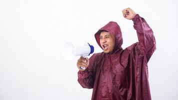 Asian man in red raincoat shout using megaphone and raising his clenched fist into the air isolated on white background photo