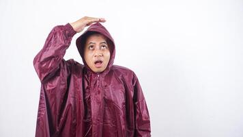 Portrait of Asian man in red raincoat covering his head with hands to shield from rain while looking up to the sky isolated on white background photo