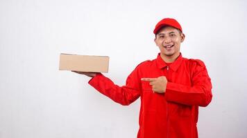Asian Delivery man in red uniform with package box parcel and pointing at it isolated on white background photo