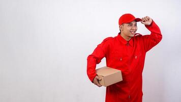 Delivery man in red uniform holding cardboard parcel box and looking at the other side isolated on white background photo